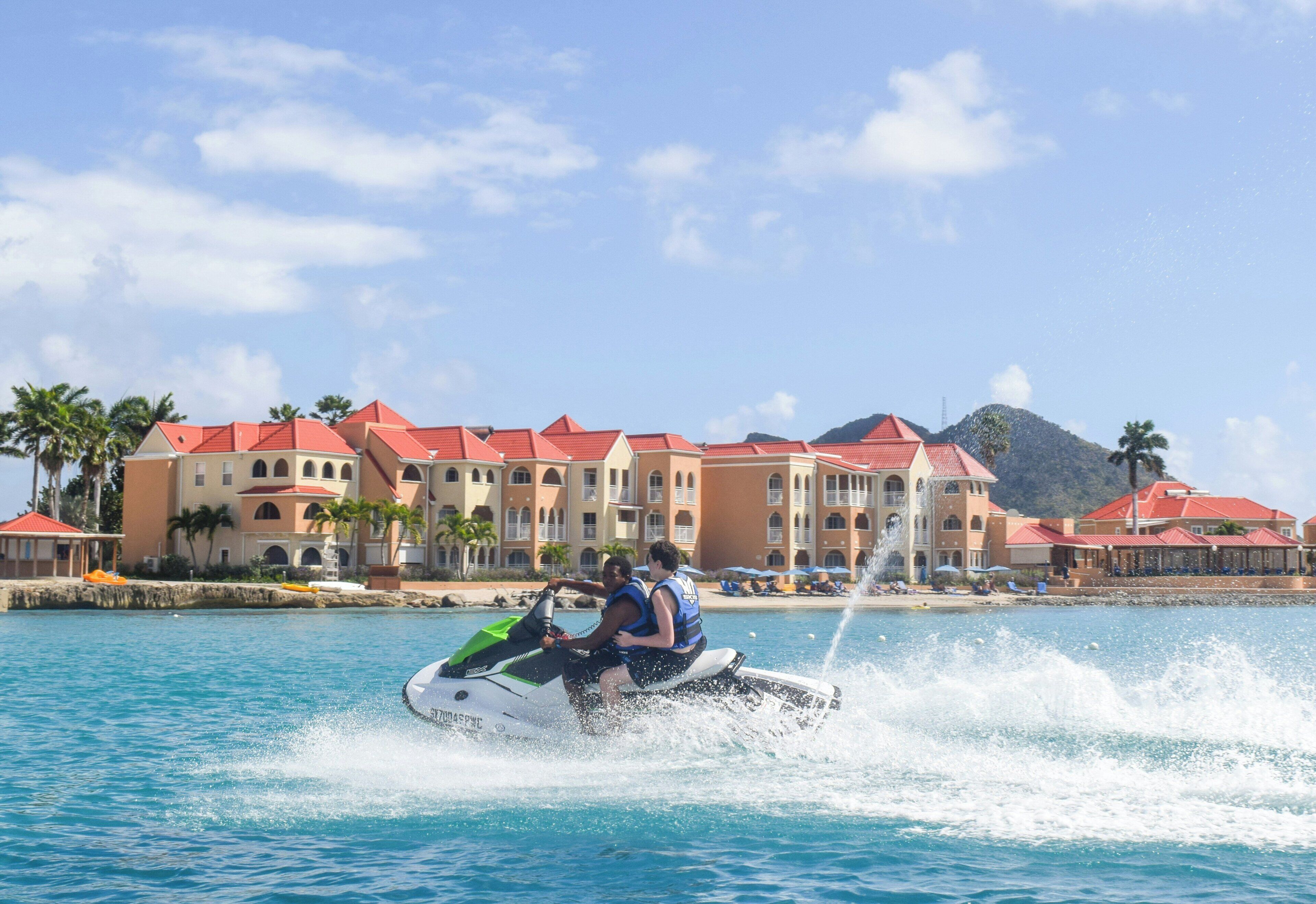 A water jet ski in motion with a resort and buildings in the background.