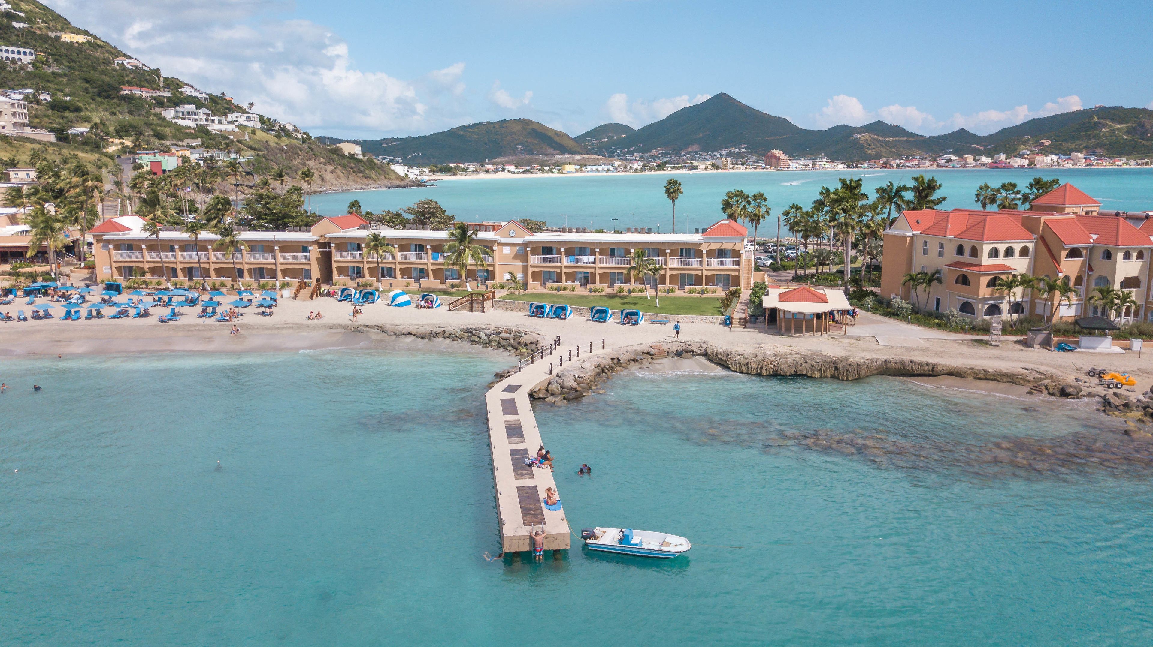 A coastal resort with a pier extending into the sea, beach umbrellas, and a boat docked at the pier.