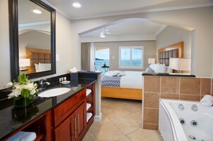 Un baño de hotel con un espejo grande, una bañera, una cama doble y vista al mar.