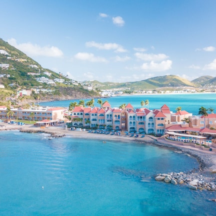 A coastal hotel with multiple buildings, a beach, and a mountainous backdrop.