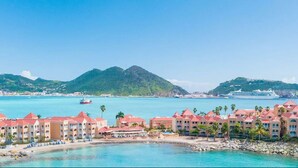 A coastal hotel with multiple red-roofed buildings, a beach, and a cruise ship in the background. - Divi Little Bay Beach Resort (Philipsburg)