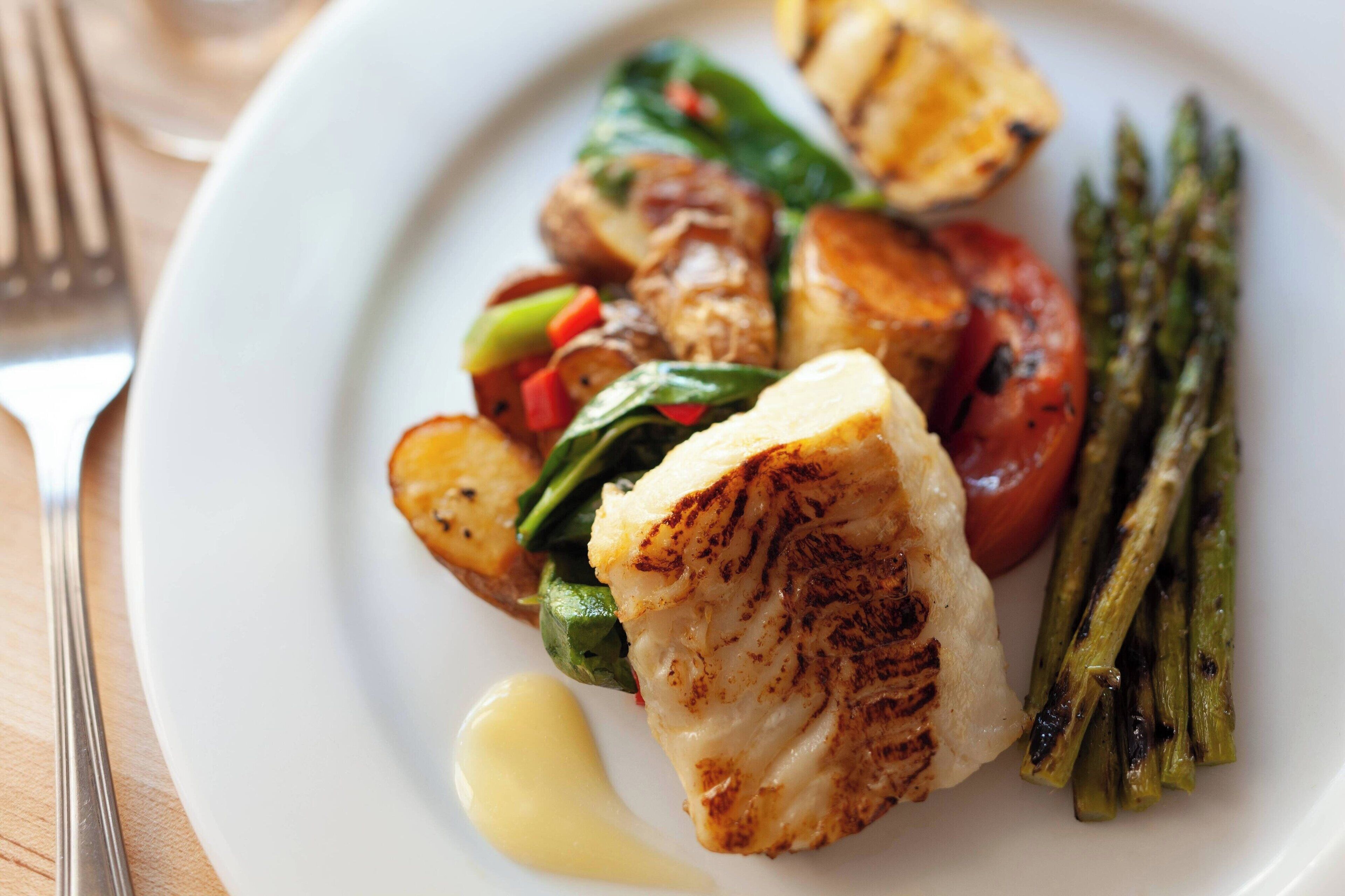 Ein Teller gegrillter Fisch, Bratkartoffeln, Spargel und gemischtes Gemüse.