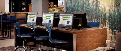 A reception desk with three computer monitors, two blue chairs, and a coffee cup on a small table.