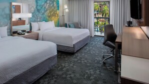 Habitación de hotel con dos camas, un escritorio, una silla, un televisor y vista a una piscina y palmeras.