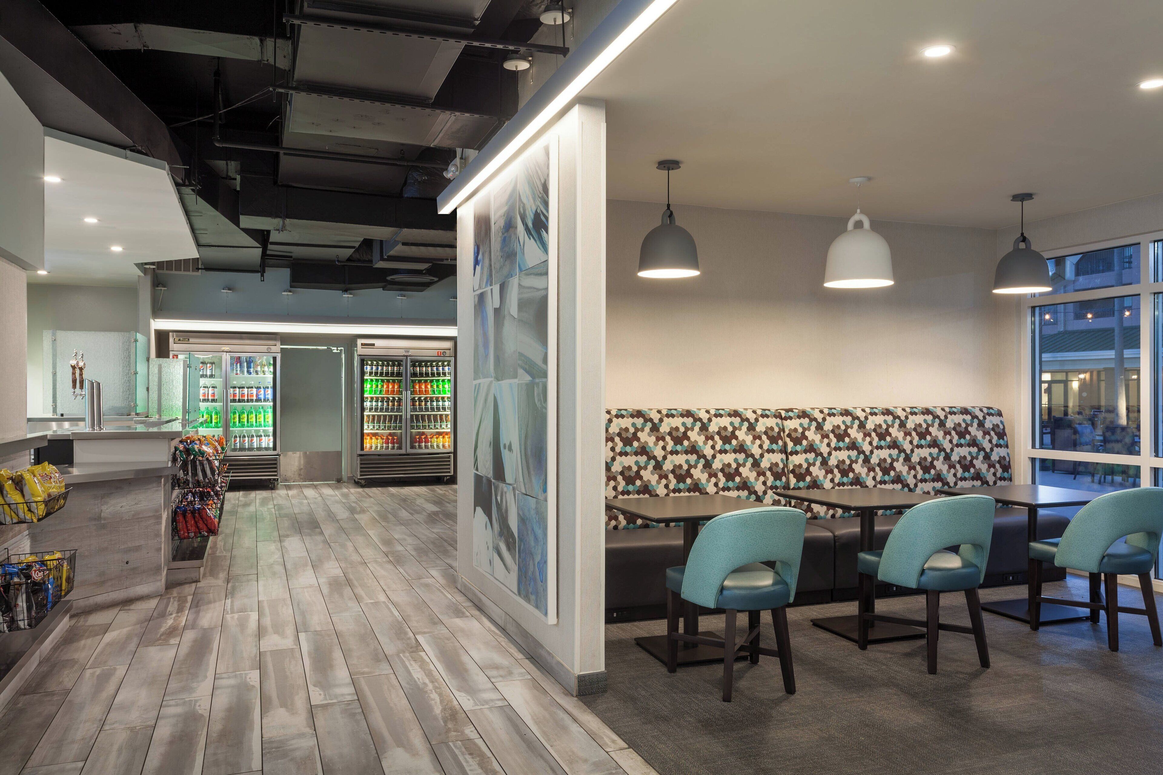 A modern interior with a wooden floor, seating area with a patterned wall, and a refrigerated display.