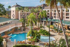 A hotel courtyard with a swimming pool, lounge chairs, and palm trees. - Courtyard Orlando Lake Buena Vista in the Marriott Village (Orlando)