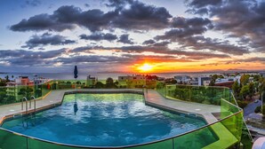 Una piscina con barandilla de vidrio, rodeada de edificios y vista al atardecer.