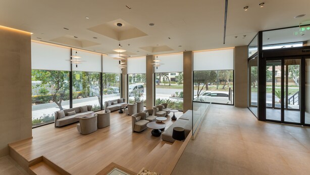 Un vestíbulo espacioso con diseño moderno, que cuenta con una zona de estar con sofás y sillones, ventanas amplias con vistas al exterior y una estética limpia y minimalista.