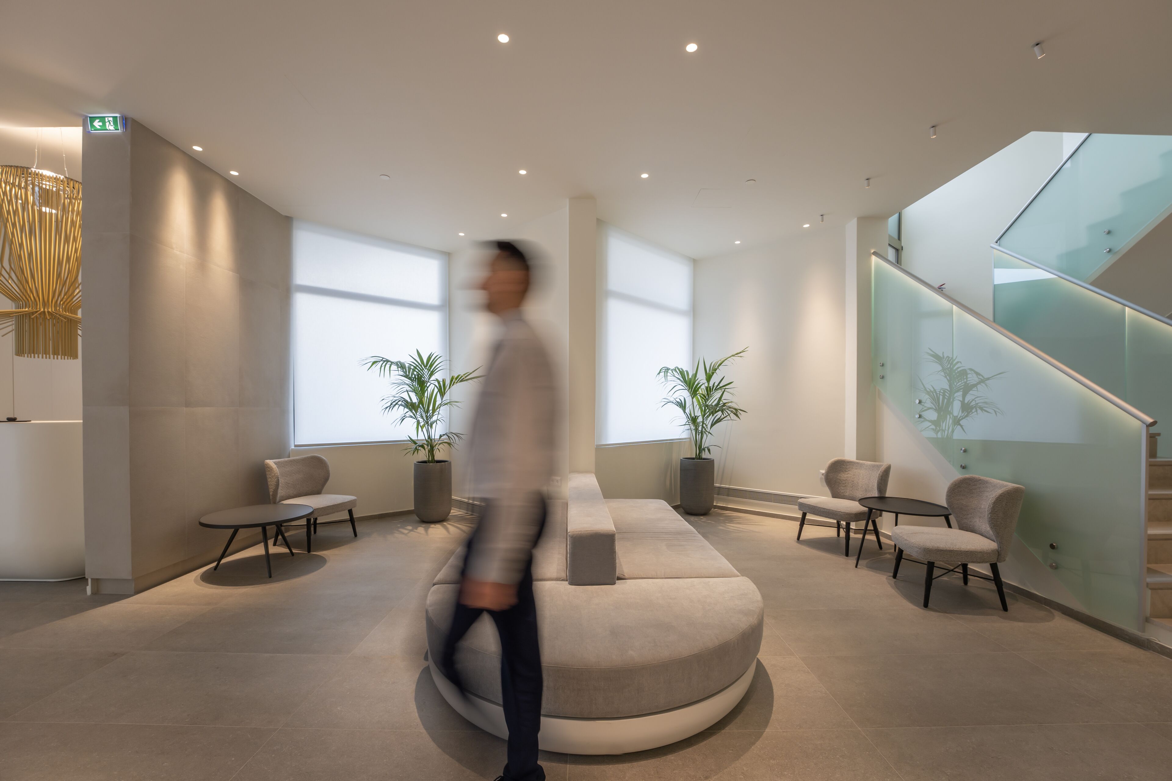 A modern lobby with a central seating area, glass railings, and potted plants.