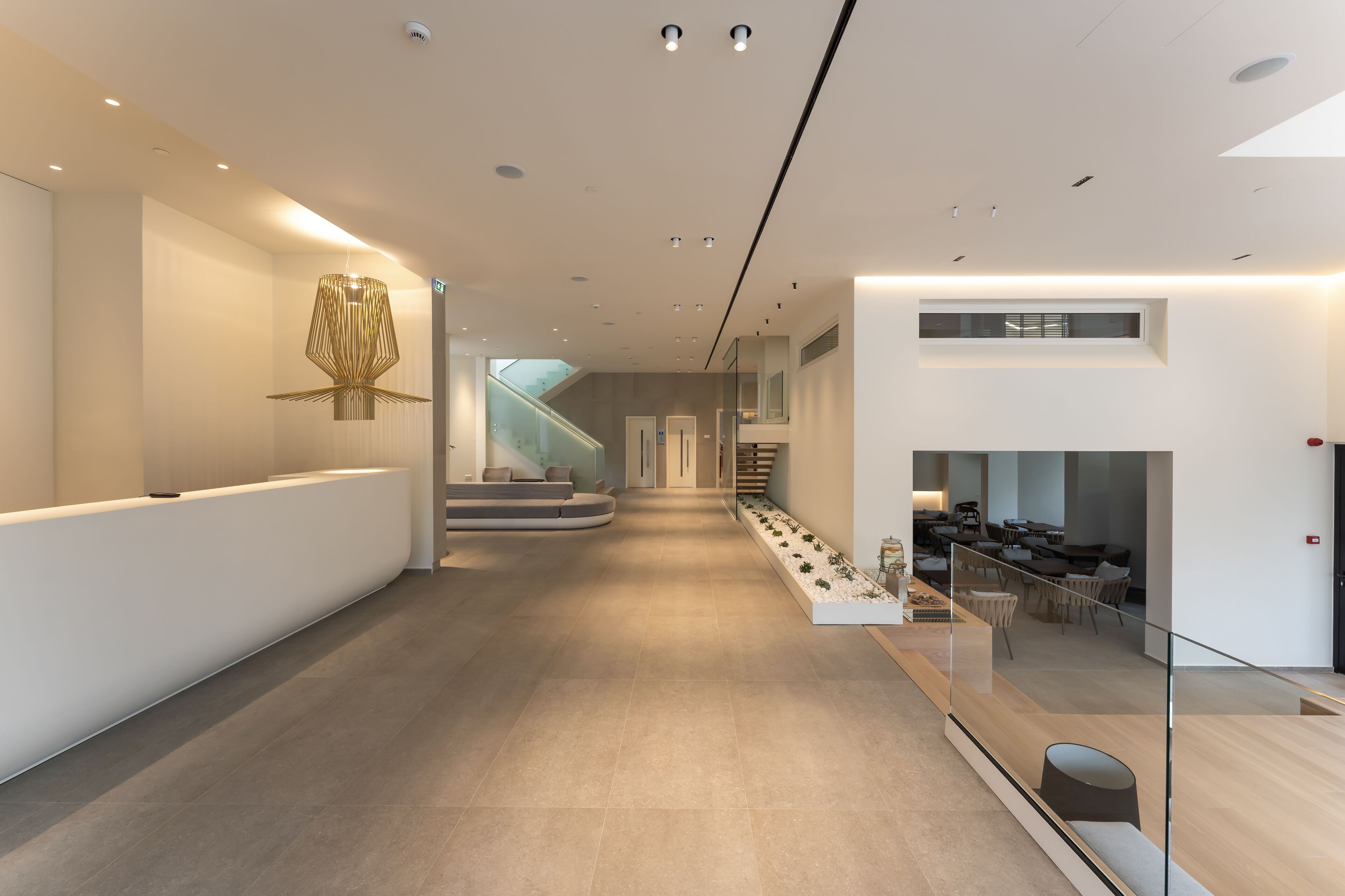 A modern interior with a reception desk, a staircase, and a seating area with a glass railing.