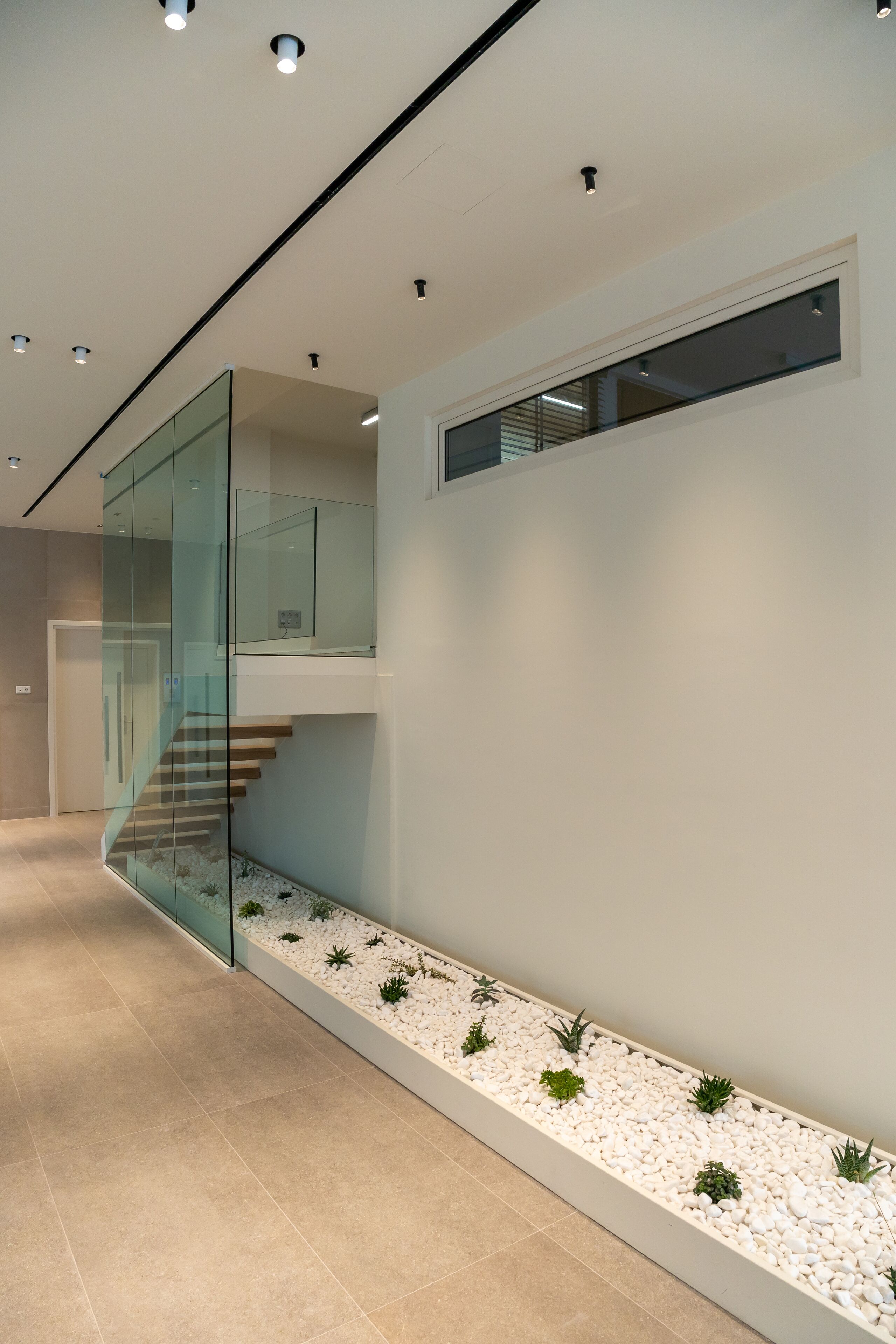 A modern interior with a glass staircase, a white pebble garden, and recessed lighting.
