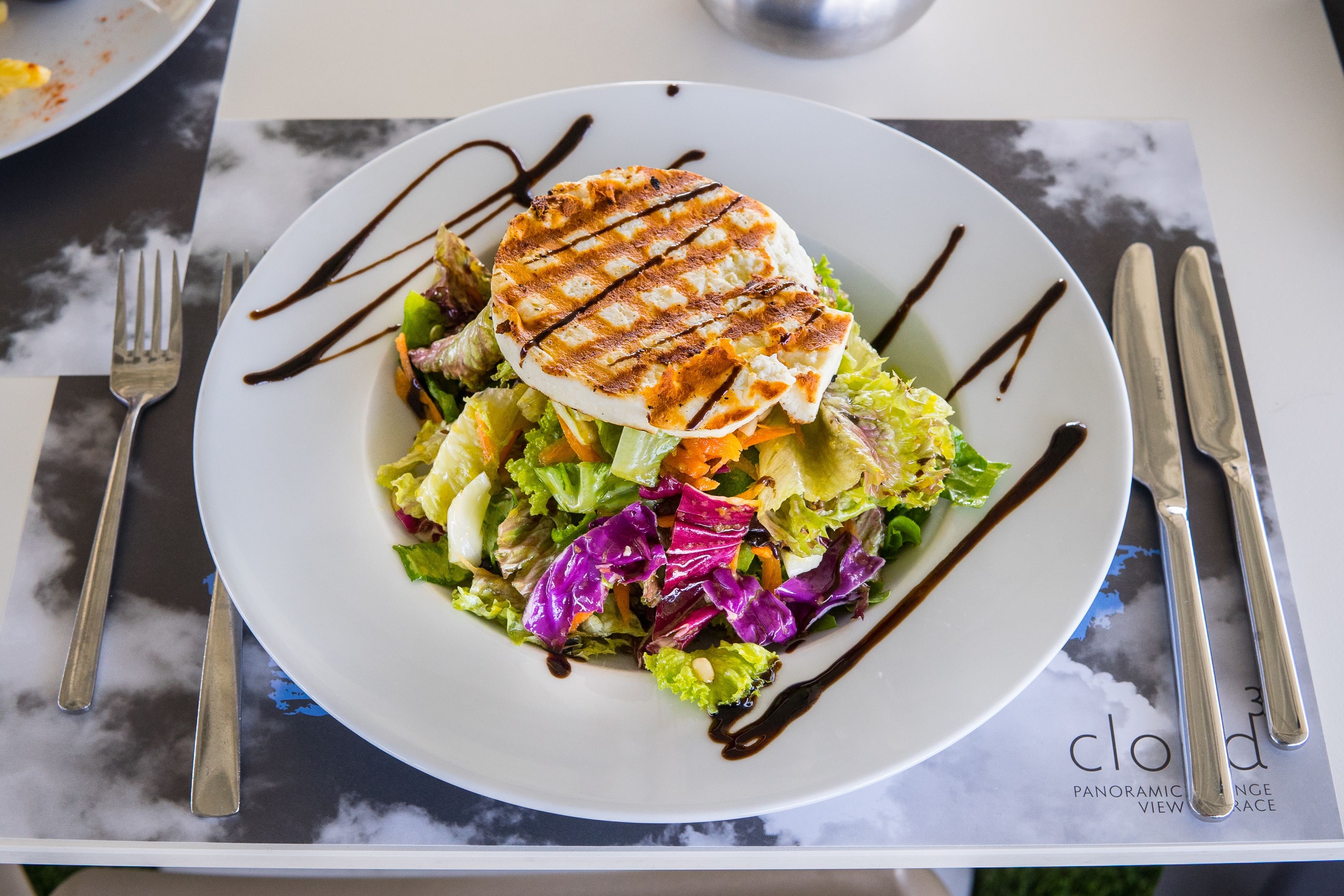 A plate of food with grilled chicken, mixed greens, and a drizzle of sauce.