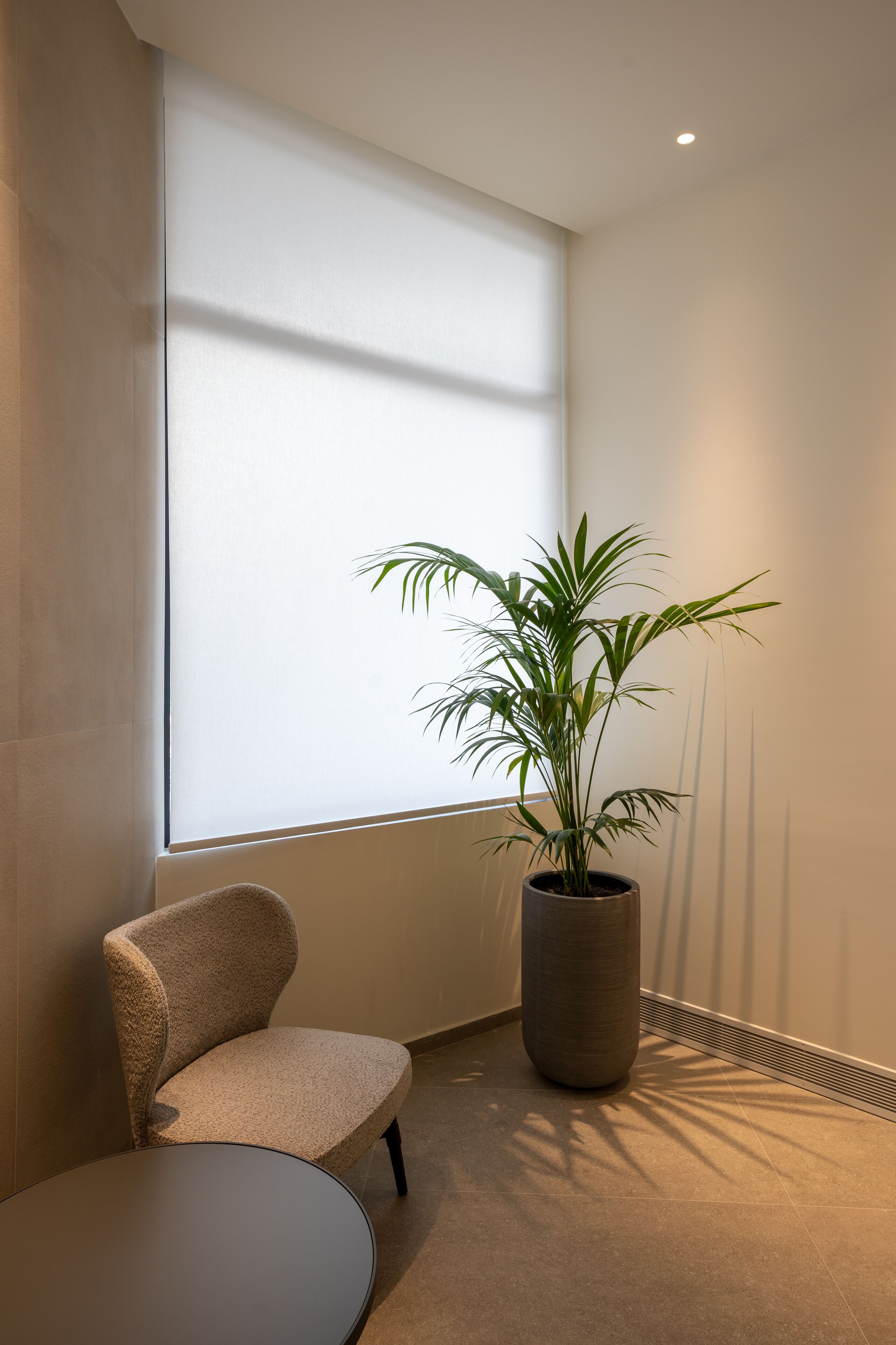 A modern room with a large window, a potted plant, a chair, and a round table.