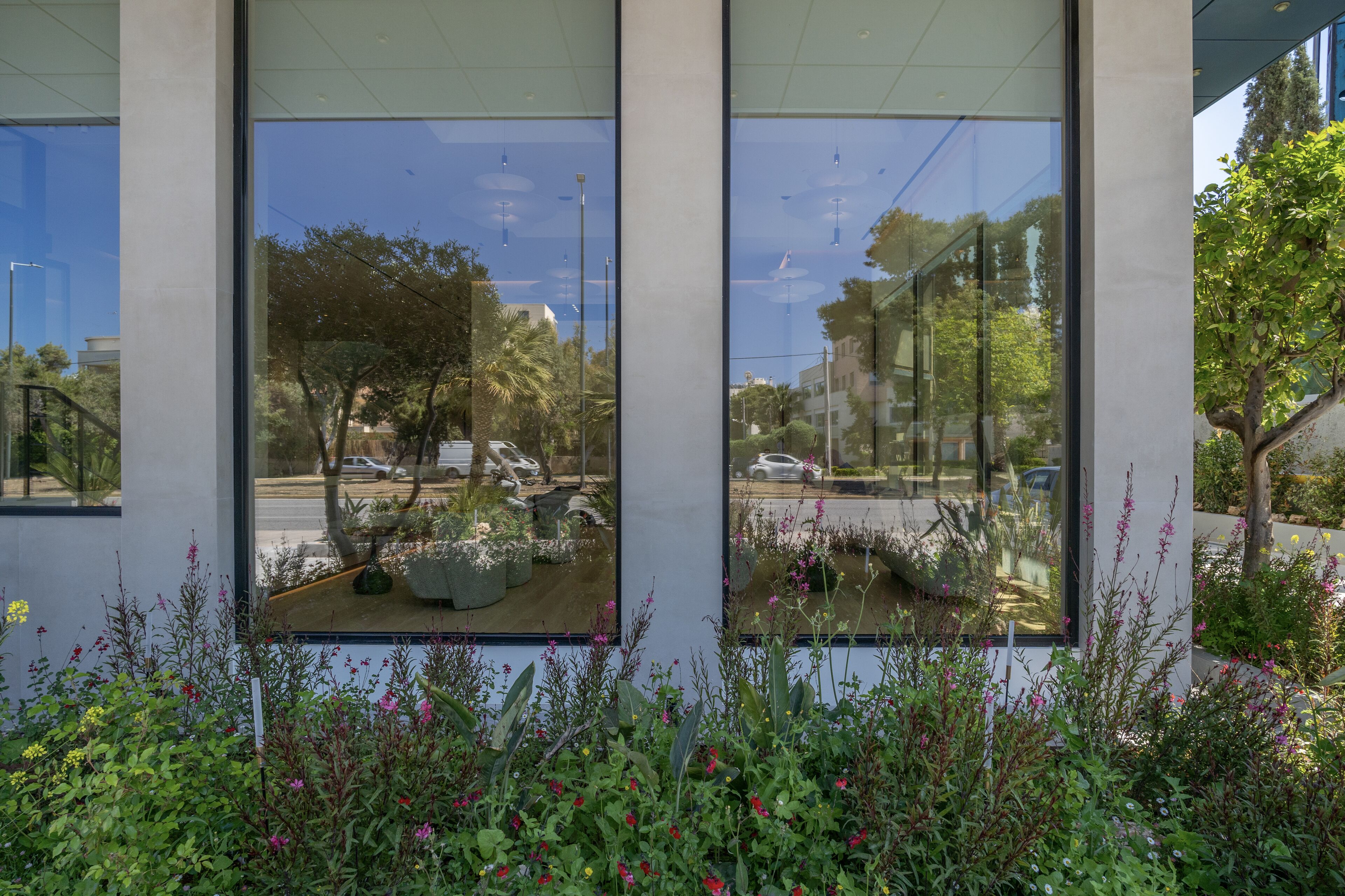 A modern building with large windows reflecting a street scene, including cars and trees.