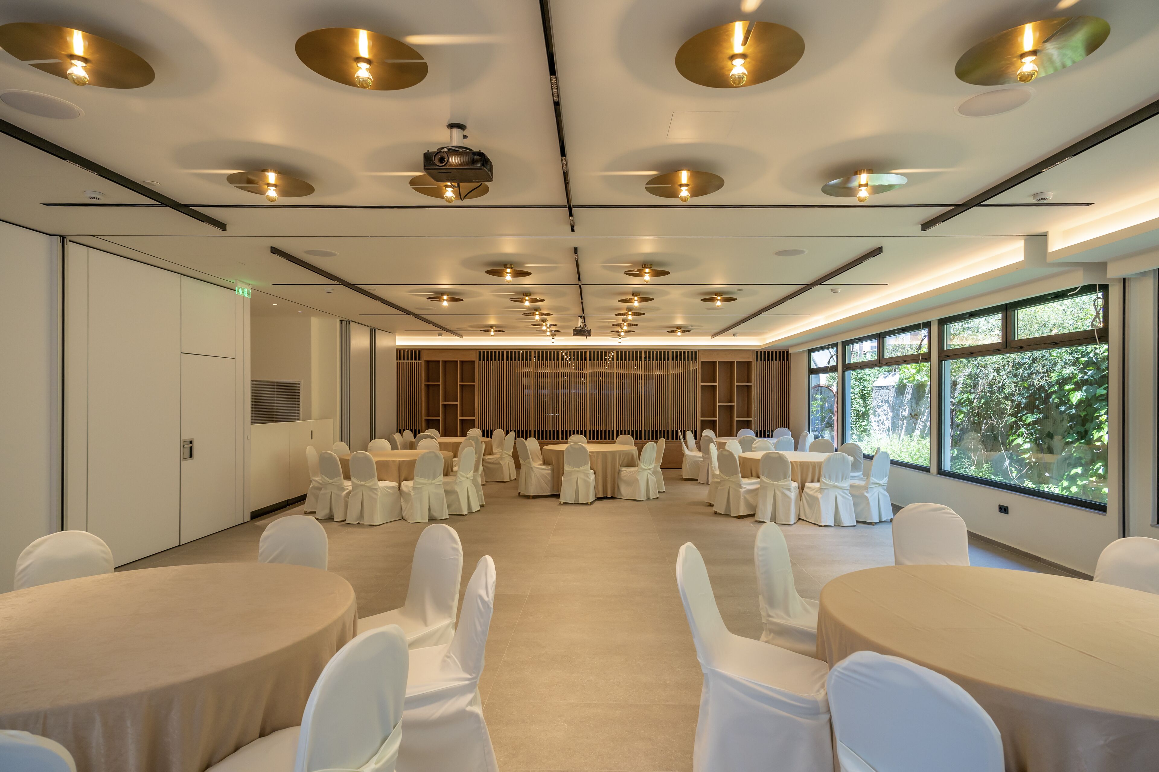 A spacious conference room with round tables and white chairs, large windows, and a modern ceiling design.