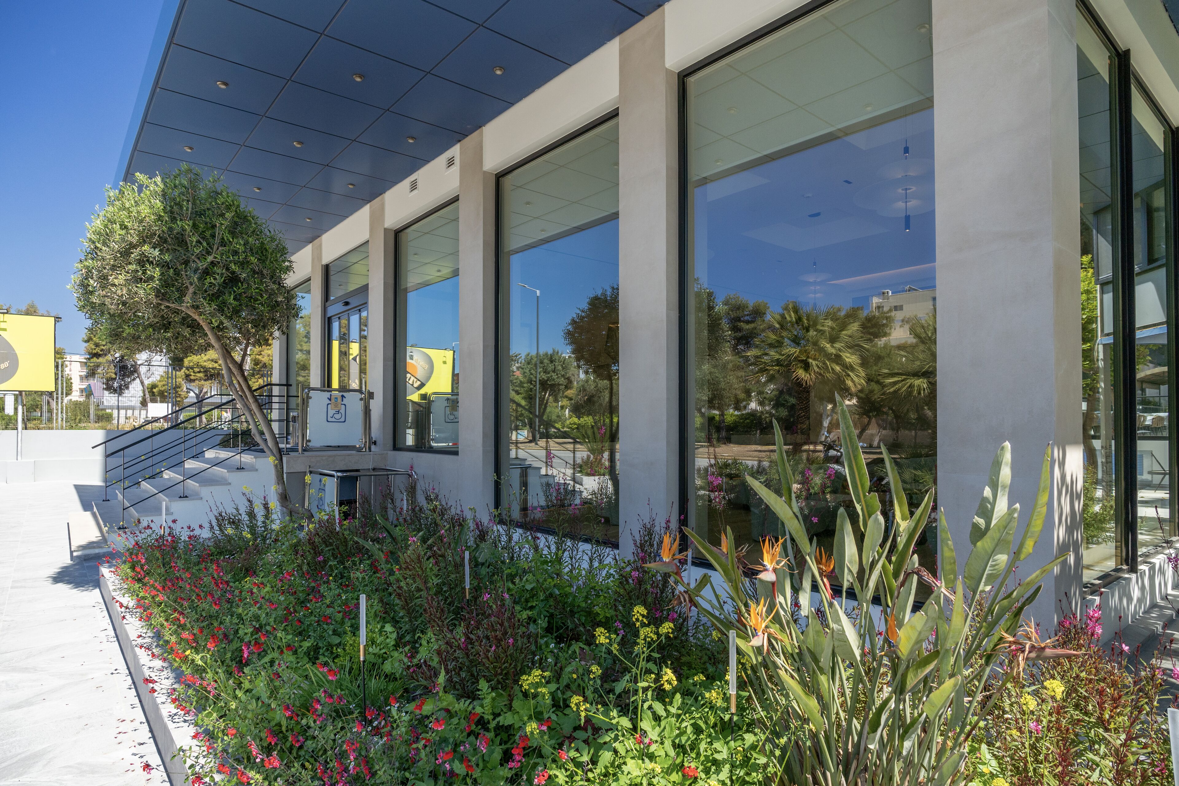 A modern building with large windows, a staircase, and a garden with various plants and flowers.