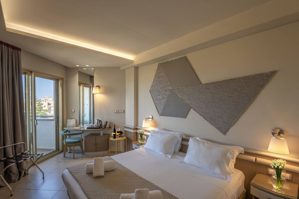 A hotel room with a large bed, a desk, a chair, and a view of the city through the window.