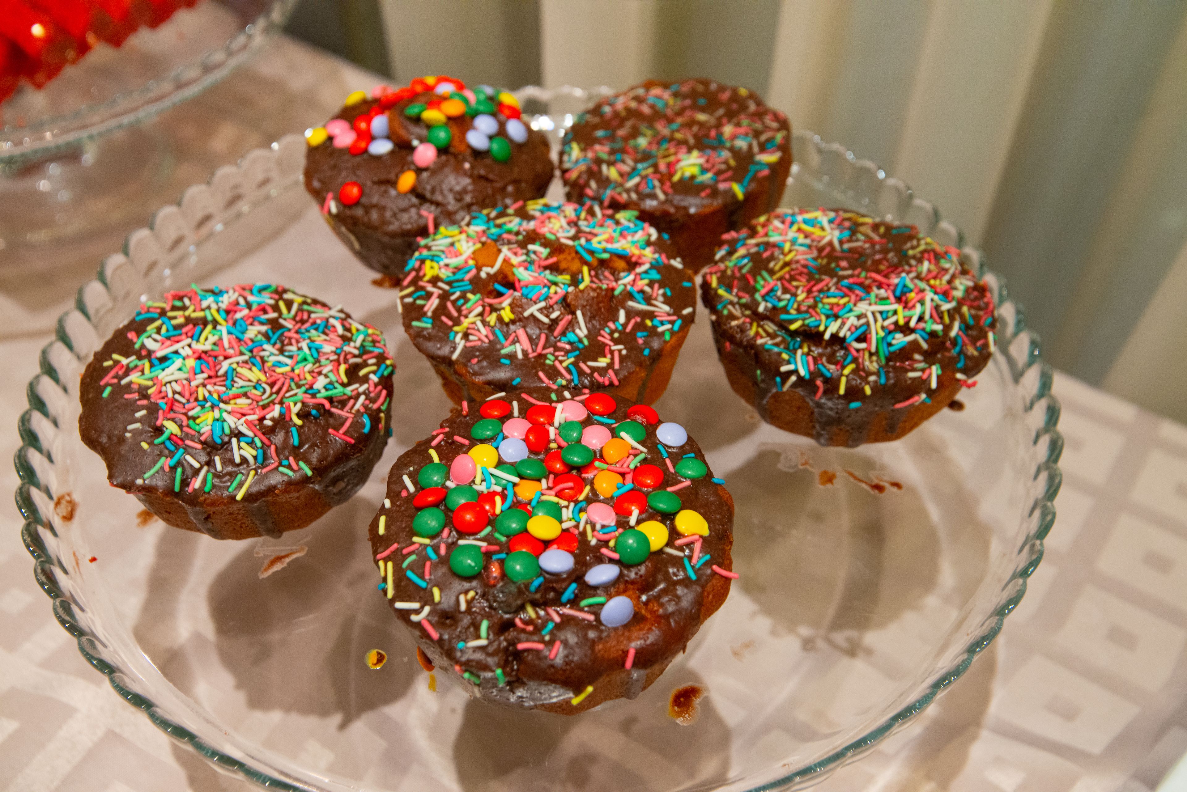 Una placa de vidrio con seis cupcakes de chocolate cubiertos de grageas coloridas y caramelos.
