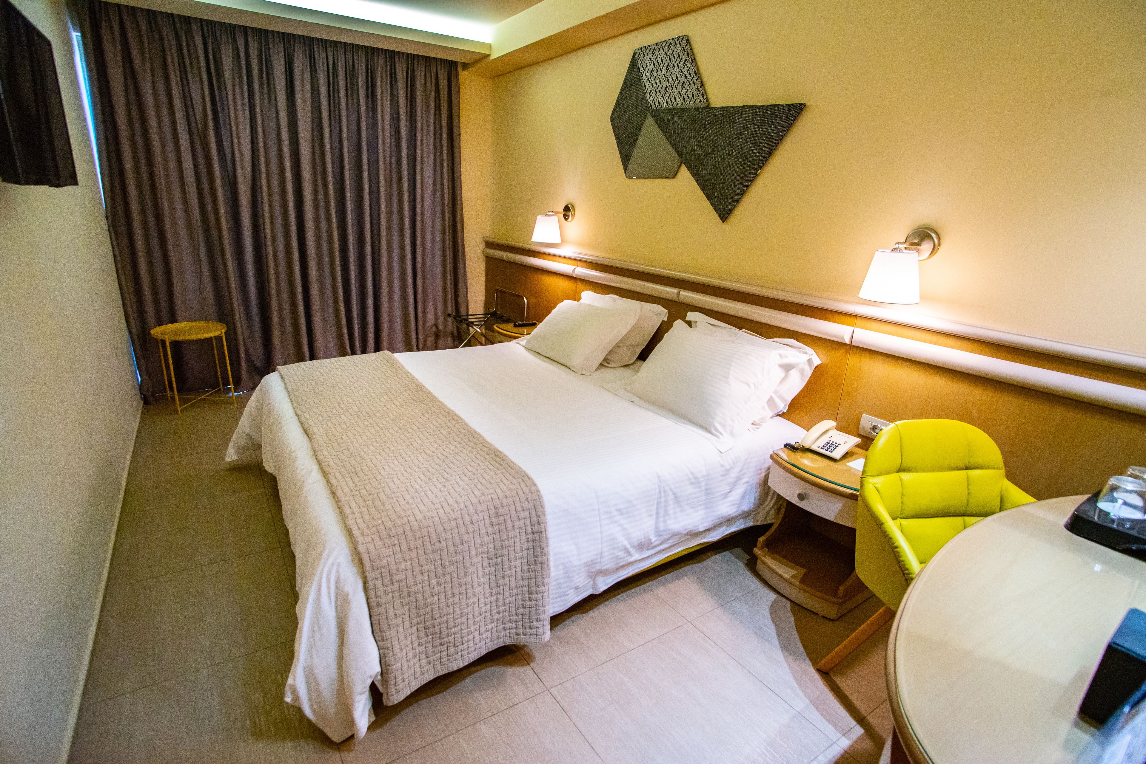 Una habitación de hotel con una cama grande, una mesita de noche con lámpara, una silla y un escritorio con teléfono.