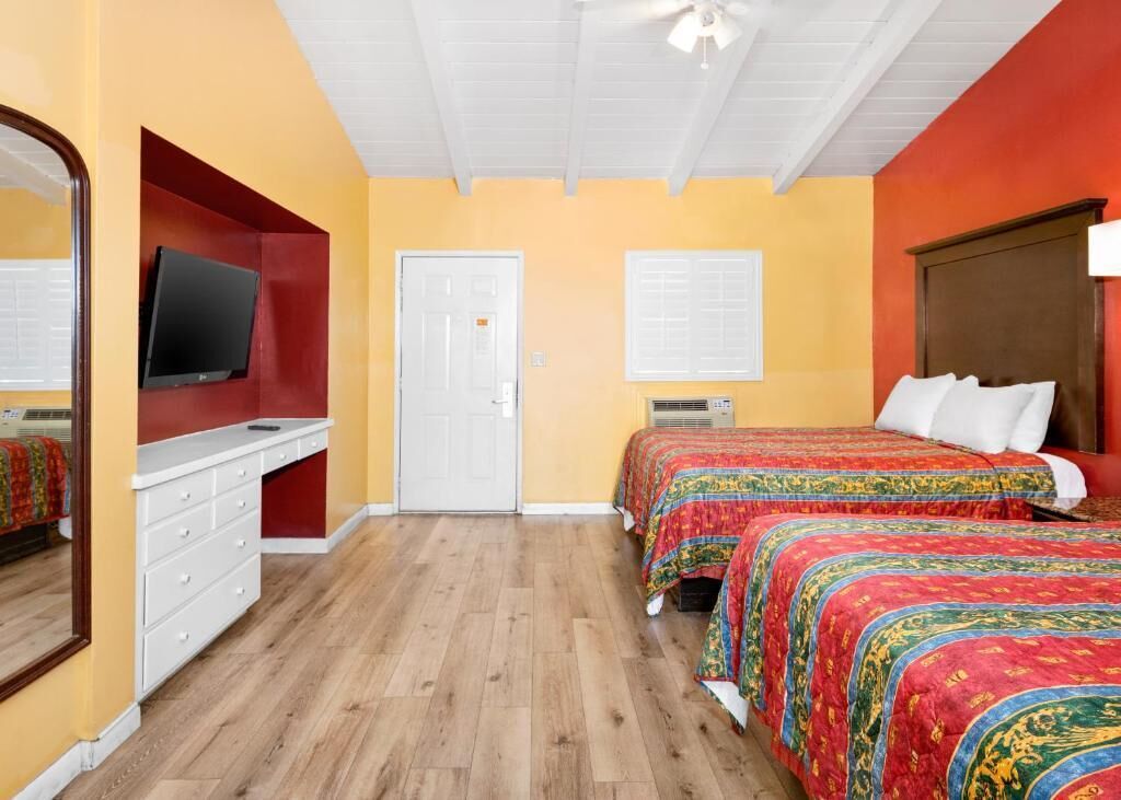 A bedroom with two beds, a TV, a dresser, and a door.
