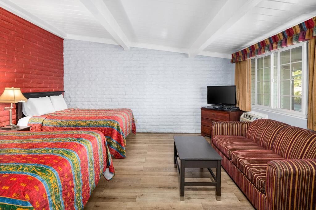 A room with two beds, a sofa, a TV, and a window with curtains.