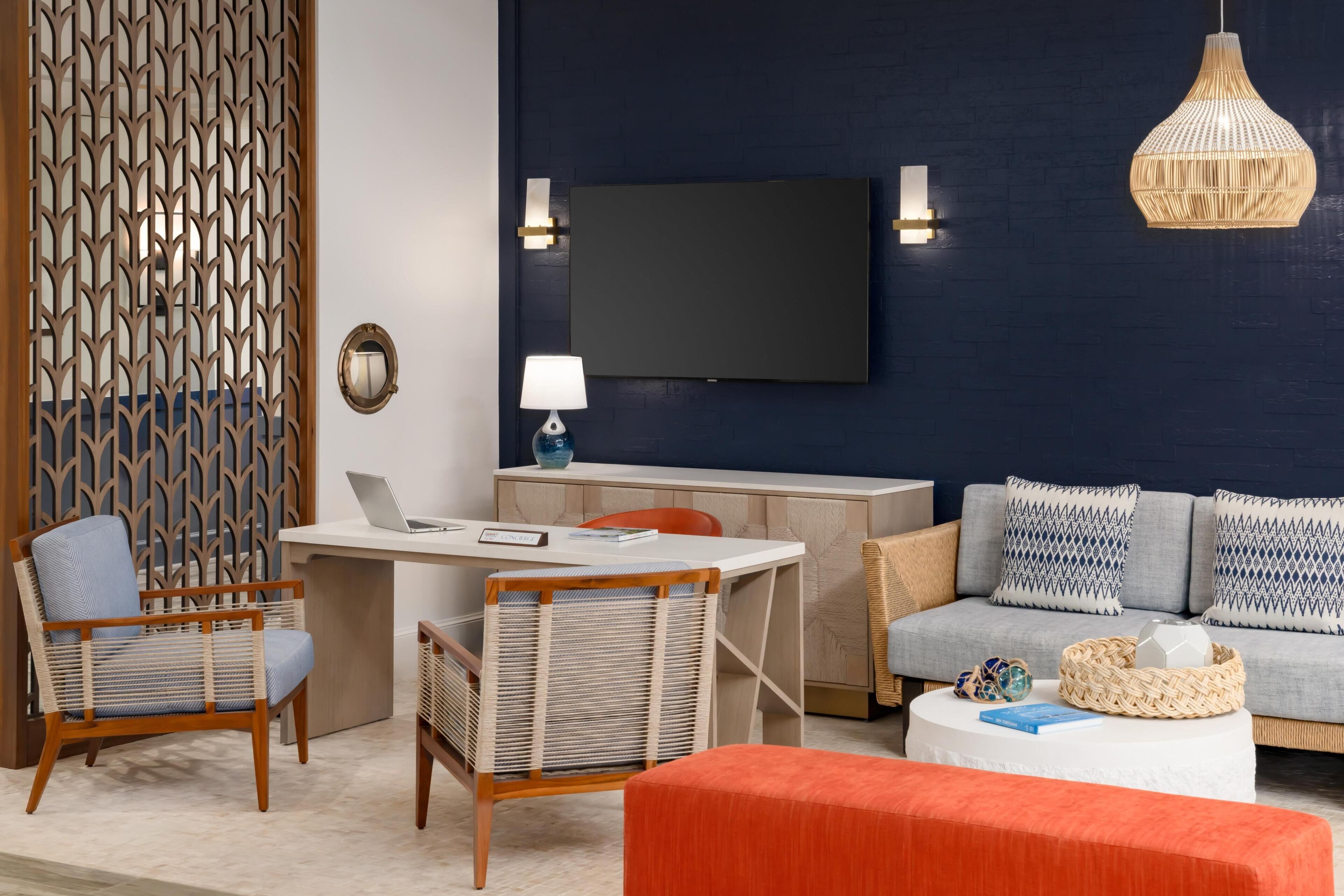 A modern living room with a flat-screen TV, a desk, two chairs, a sofa, and a hanging light fixture.