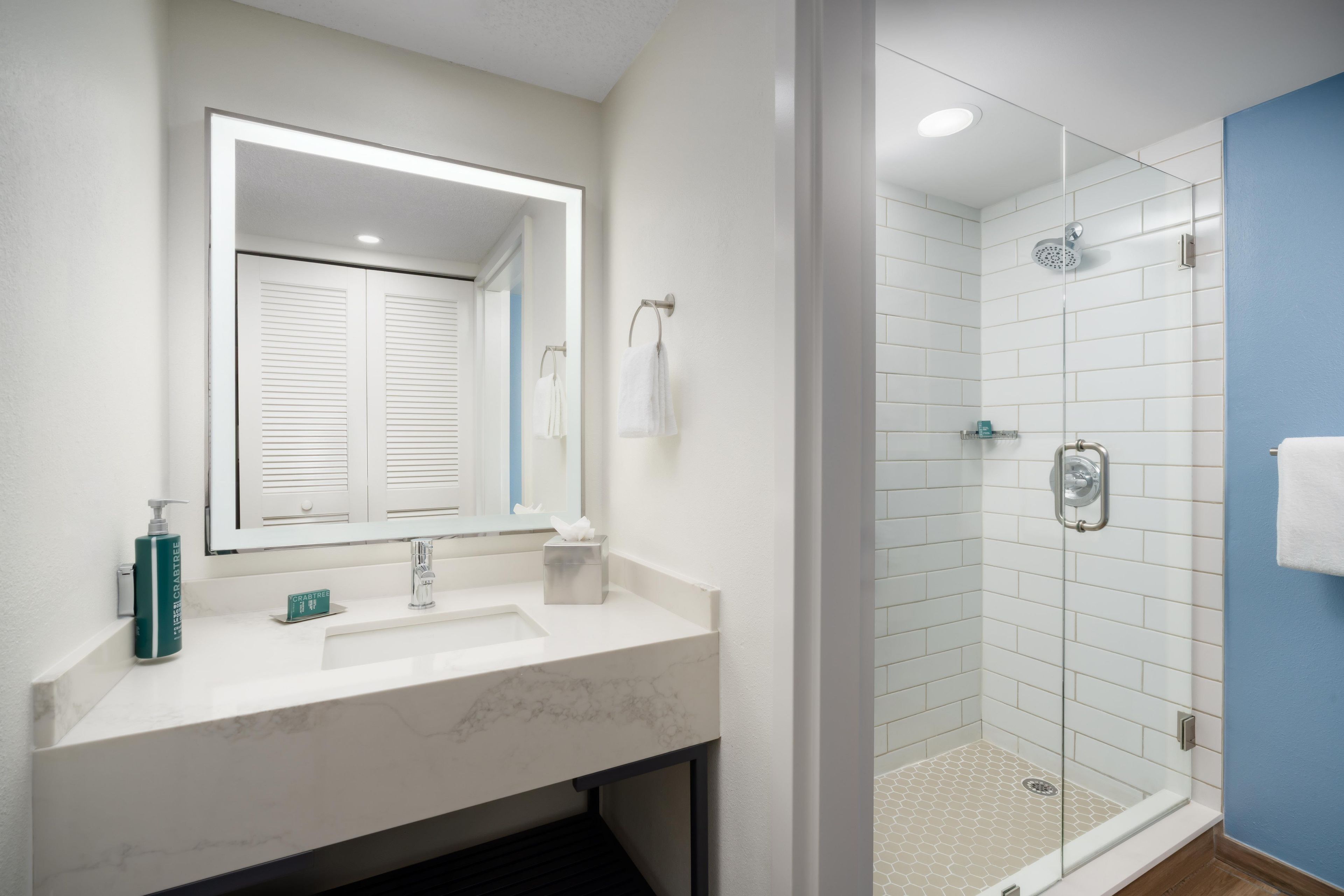 Ein Badezimmer mit einem weißen Waschbecken, einem Spiegel, einer Duschkabine und einer blauen Akzentwand.