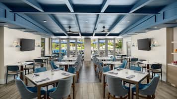 Un espace repas moderne doté de plusieurs tables et chaises, de grandes fenêtres et de ventilateurs de plafond.