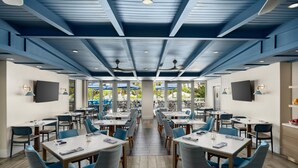 Un vaste espace intérieur aménagé en salle à manger, avec des tables et des chaises, des ventilateurs de plafond et de grandes fenêtres.