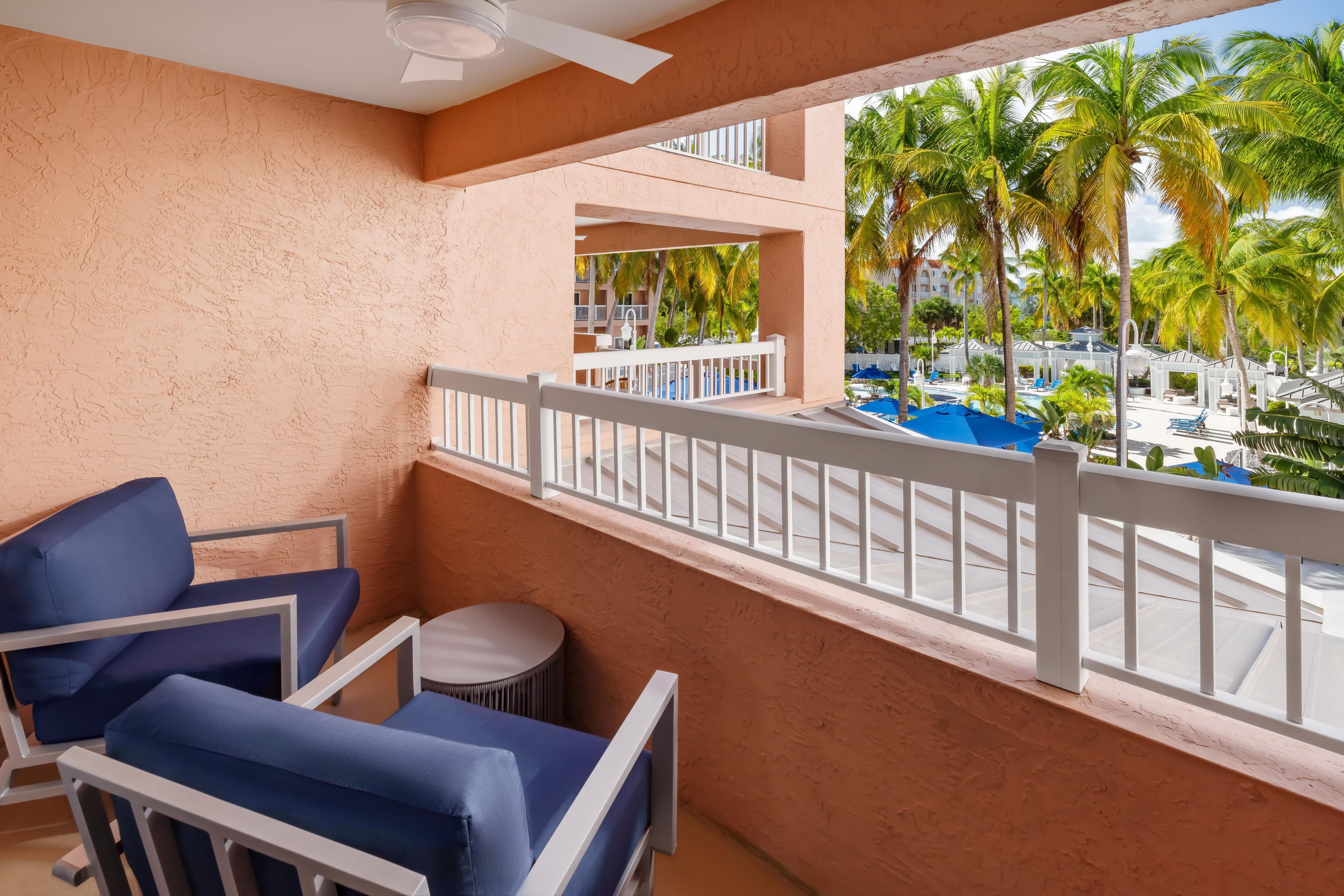 Un balcon avec vue sur une piscine et des palmiers, comprenant une chaise et une petite table ronde.