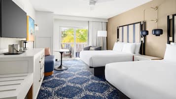 A hotel room with two beds, a desk, a chair, a TV, and a balcony with a view of palm trees.