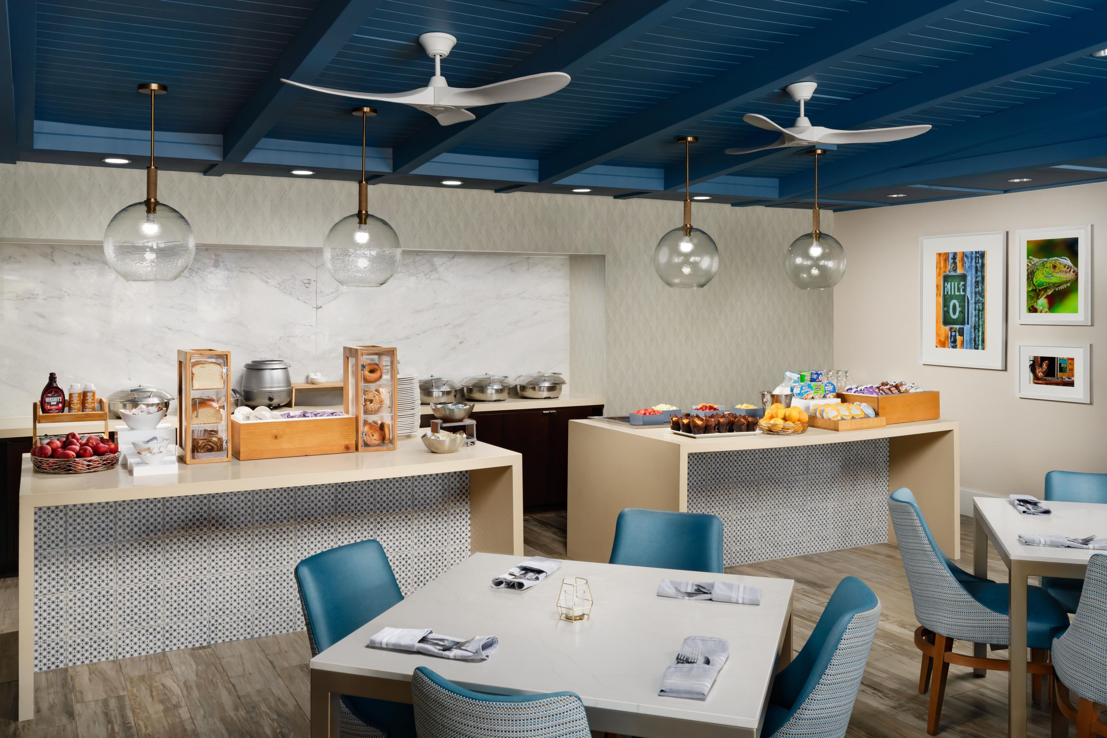Un restaurant moderne avec un comptoir central, des chaises bleues et des ventilateurs de plafond.