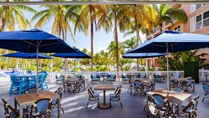Une terrasse extérieure avec des tables et des chaises, des parasols et des palmiers.