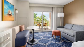 A hotel room with a sofa, a small table, a lamp, and a balcony with chairs.