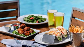 Una mesa con comida y bebidas, una piscina al fondo y una silla de madera.