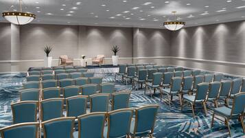 A conference room with rows of chairs, a stage with a table, and two chandeliers.