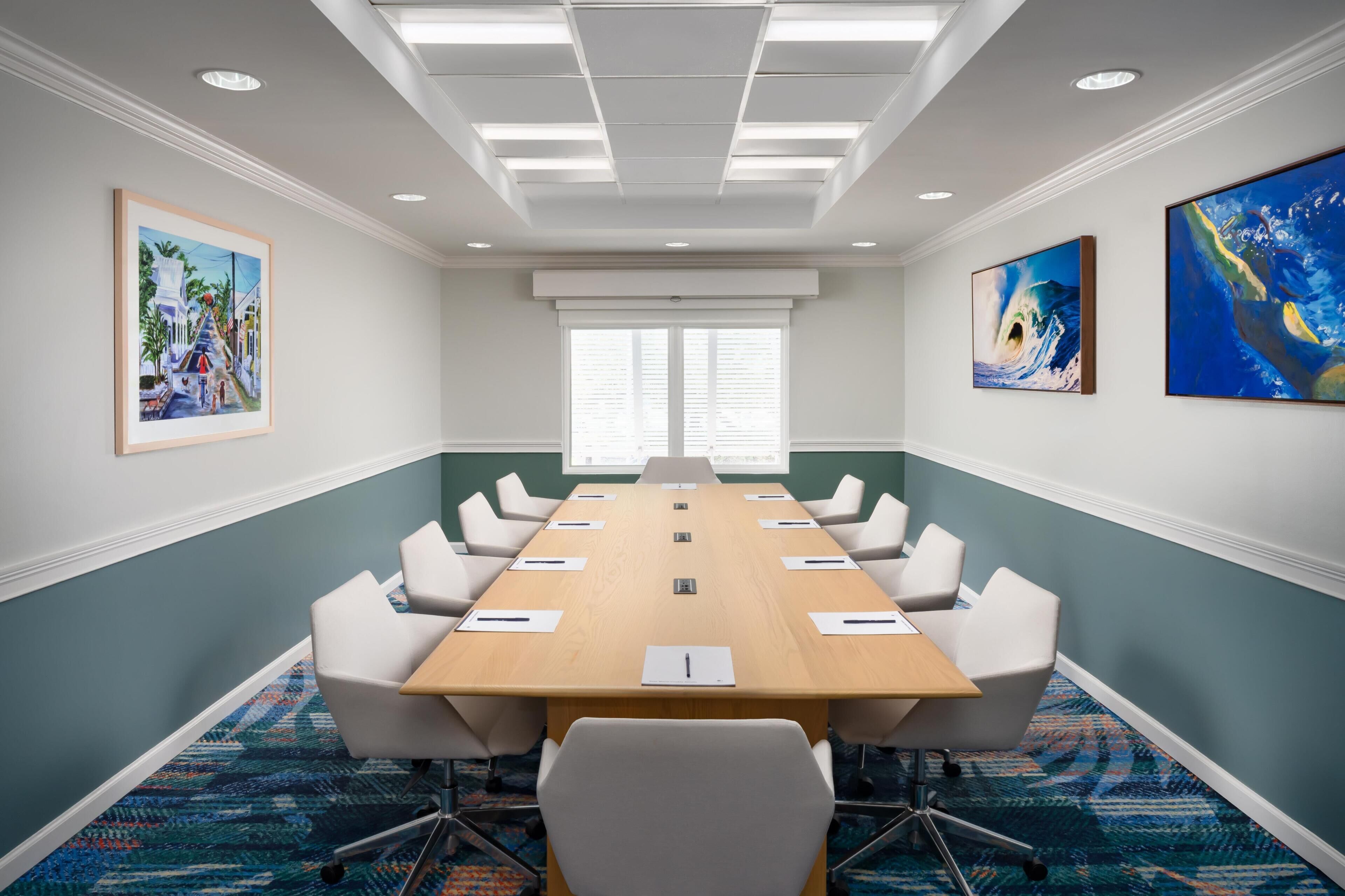 A conference room with a long table, white chairs, and artwork on the walls.
