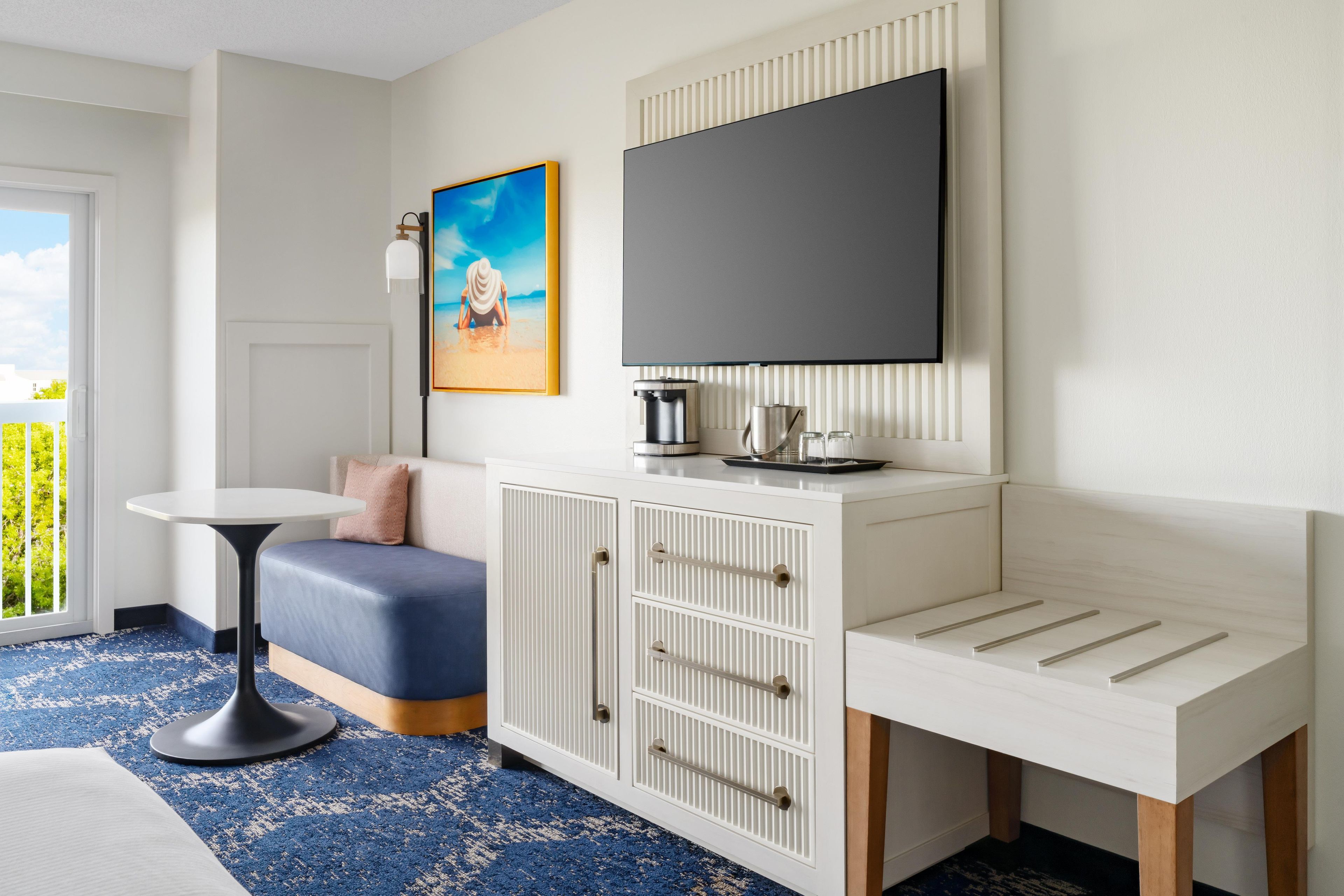Una habitación moderna con un armario blanco, un televisor de pantalla plana, una mesita y un banco.