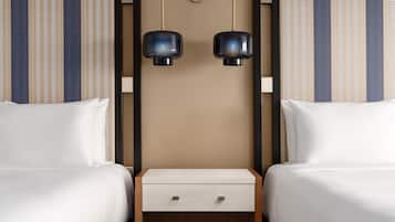 Quarto de hotel com duas camas, uma mesinha de cabeceira e duas luminárias fixadas na parede.