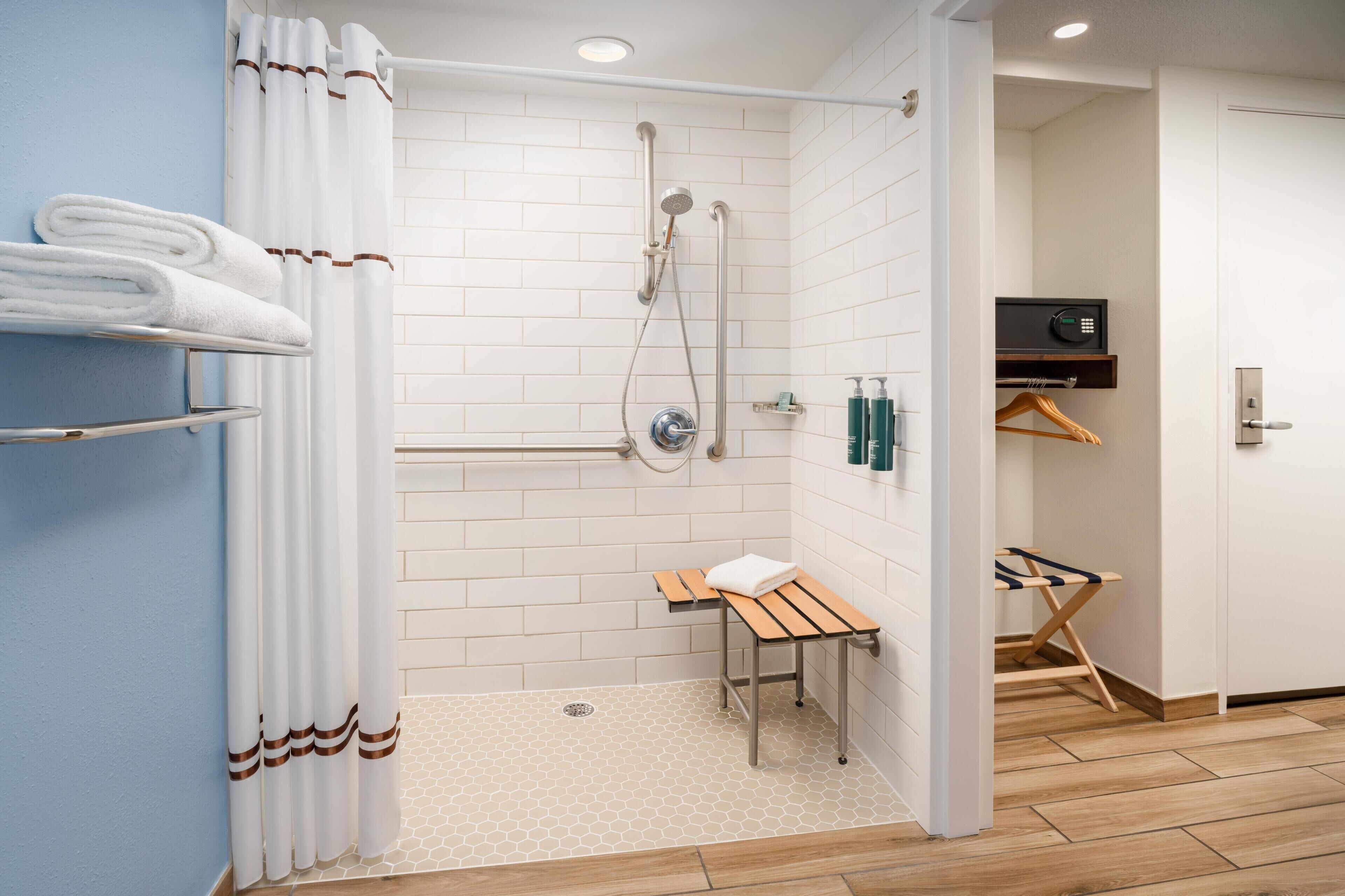 Un baño moderno con ducha, perchero, una mesita y un banco de madera.
