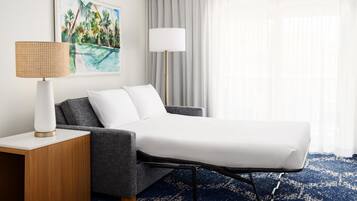 A hotel room with a bed, a nightstand, a lamp, a painting, and a window with curtains.