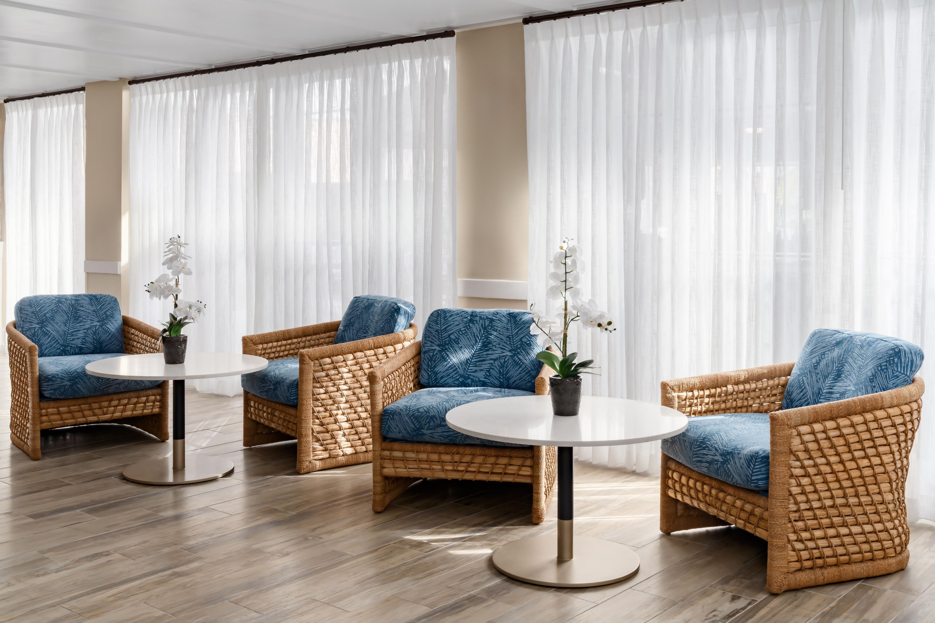 A room with wicker furniture, including two sofas and two armchairs, each with a round table. There are potted plants on the tables.
