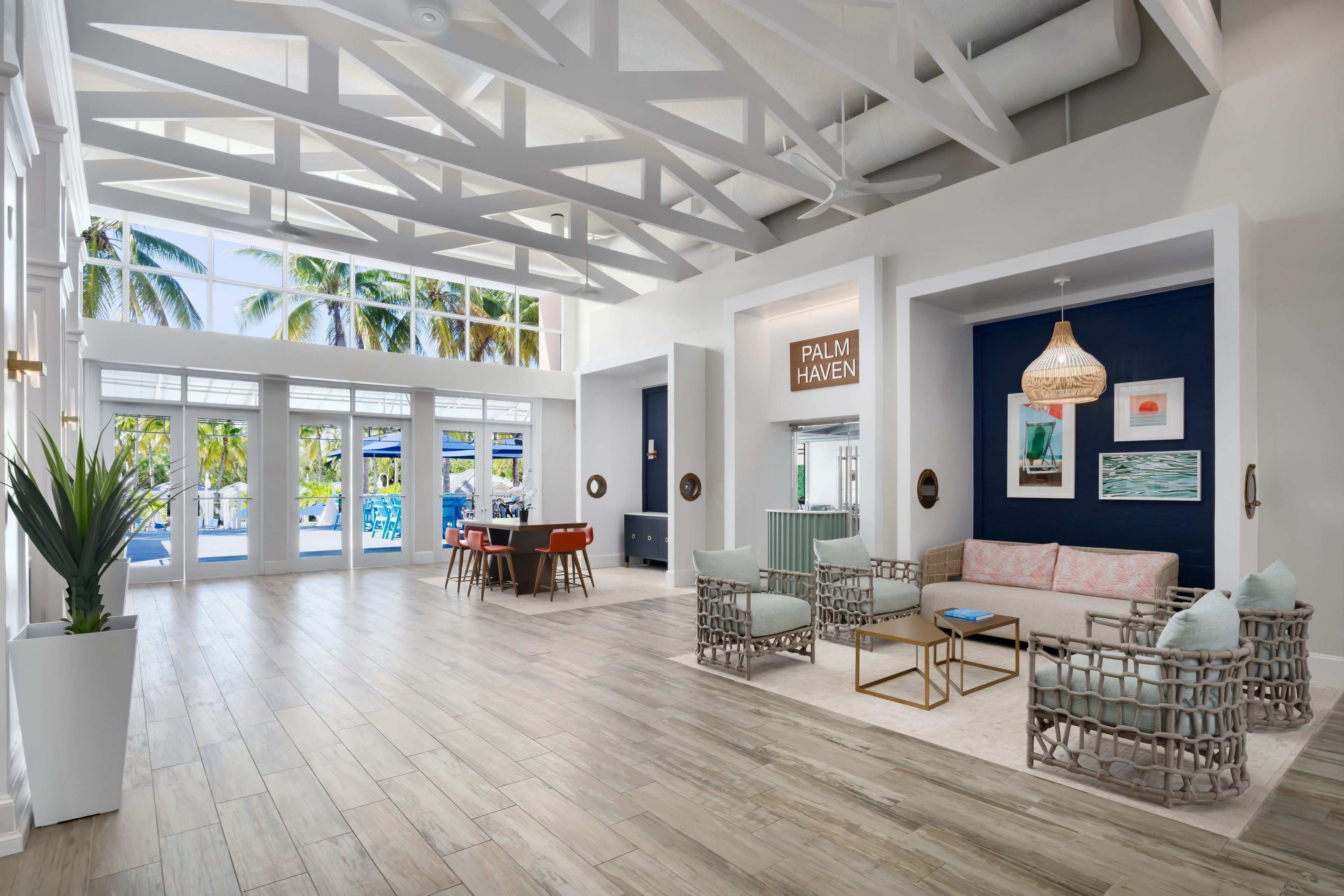 A spacious room with a high ceiling, large windows, and a view of palm trees.