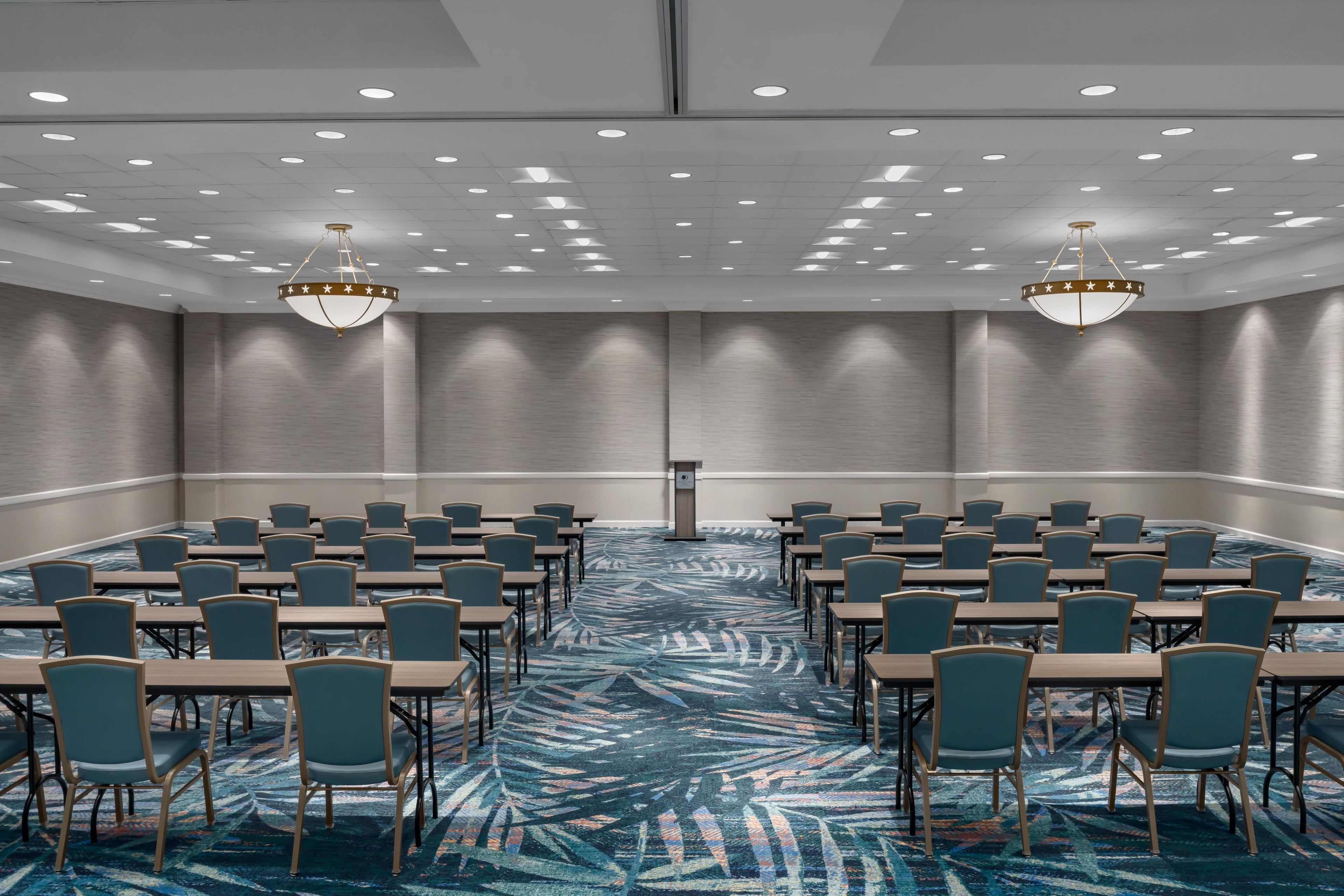 Un salón de conferencias con alfombra estampada, varias mesas, sillas y dos candelabros.