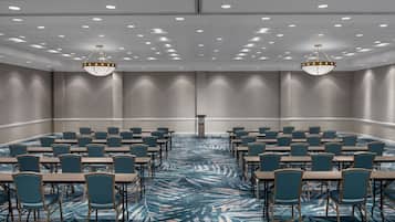 Un salón de conferencias con alfombra estampada, varias mesas, sillas y dos candelabros.