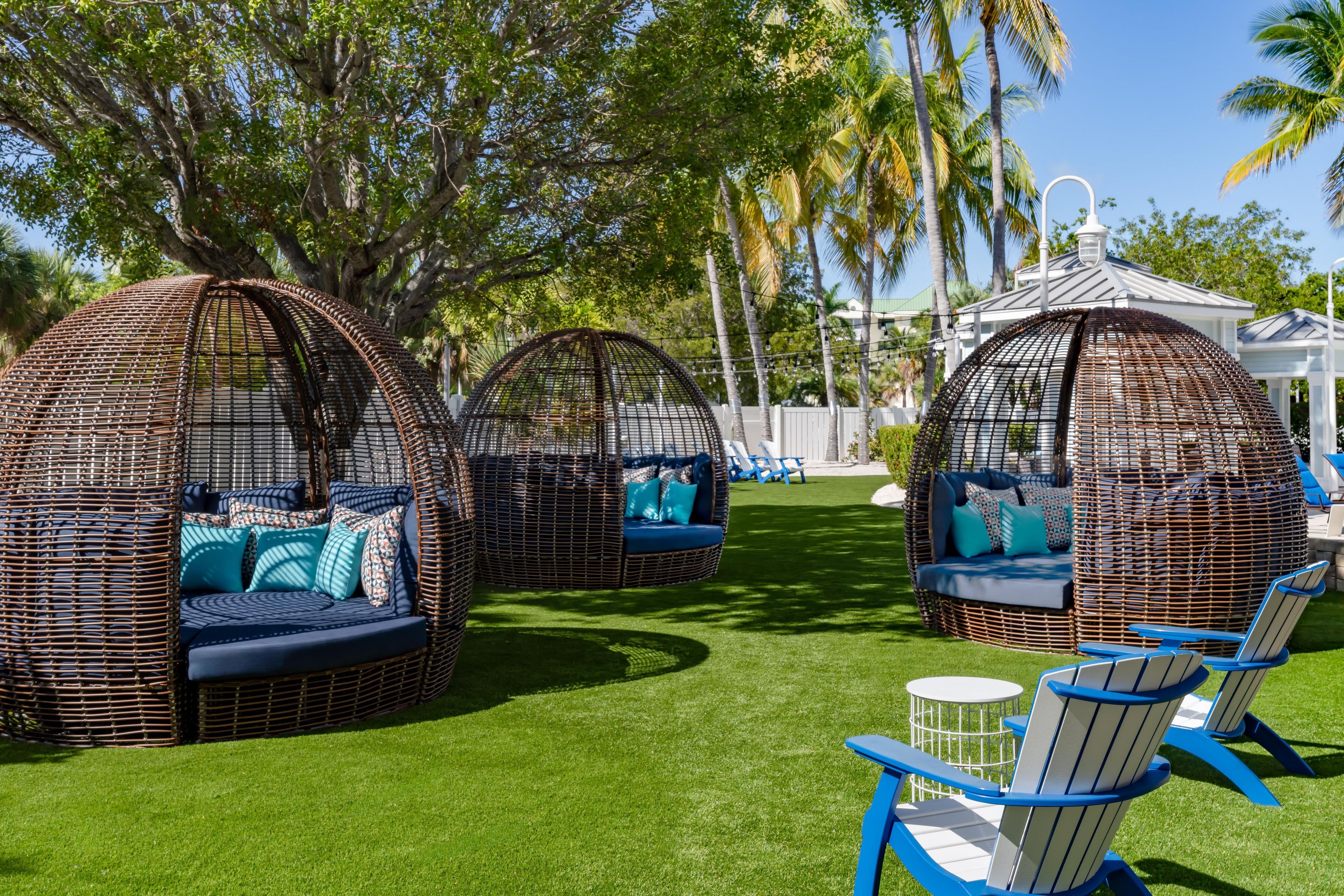 Outdoor wicker furniture with cushions, a lawn, and palm trees.