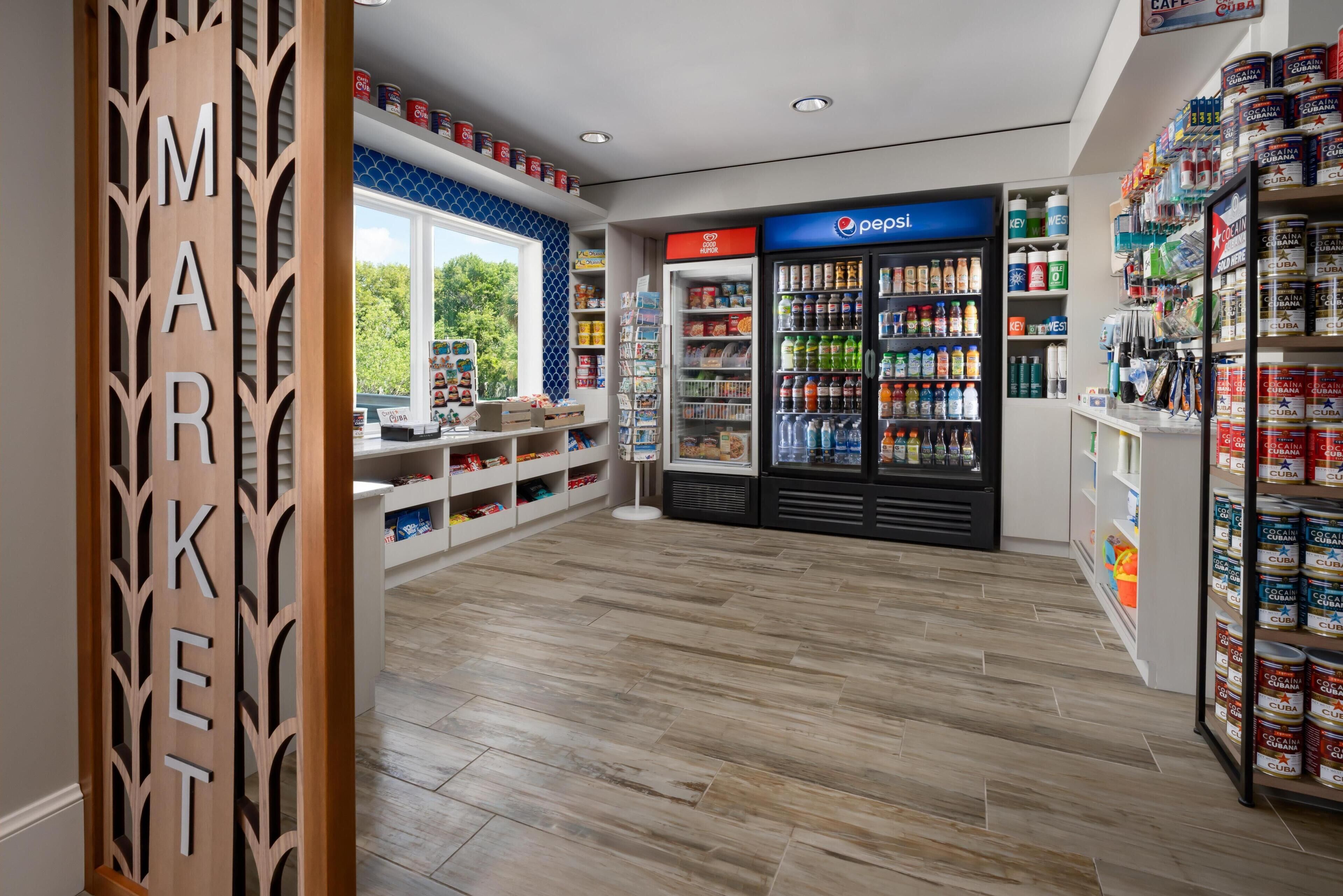 Un vaste espace dédié à la vente, avec un réfrigérateur Pepsi, des étagères remplies de conserves et un panneau en bois sur lequel est inscrit le mot « MARCHÉ ».