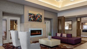 A modern lobby with a fireplace, seating area, and abstract art. - Hilton Garden Inn Phoenix Airport (Phoenix)