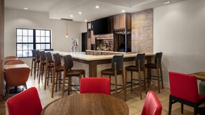 A modern bar area with a long counter, multiple bar stools, and a television screen. - Hilton Garden Inn Phoenix Airport (Phoenix)