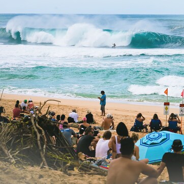 A beach with people watching surfers, a lifeguard, and beach chairs.